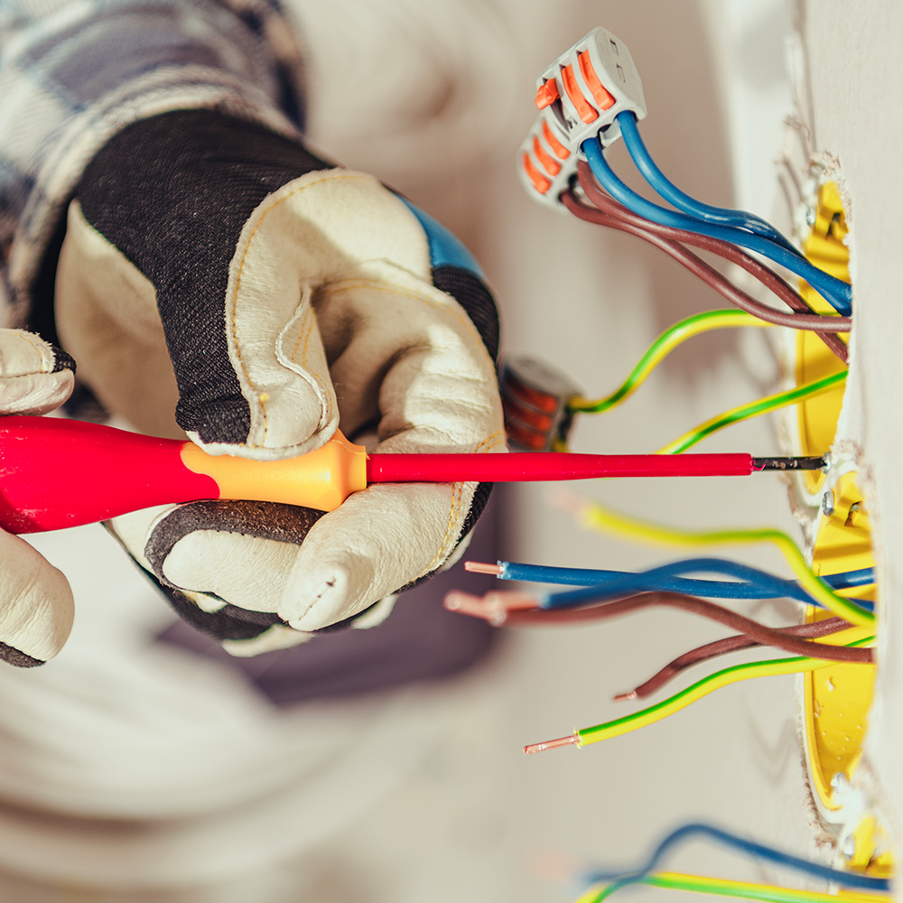 Hände eines Elektrikers halten einen Schraubenzieher und befestigen Steckdose in der Wand